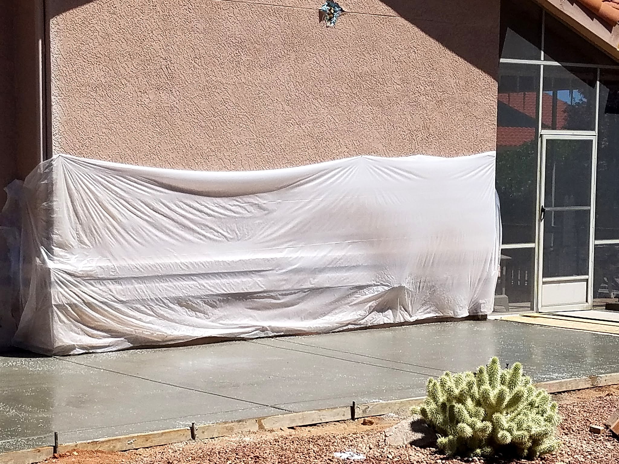 New slab along a house wall with plastic protecting the stucco